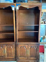 Front view of the traditional wooden shelf unit, showing open shelves and two cabinet doors with arched detailing and brass handles.