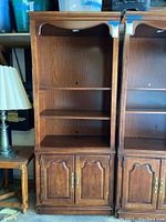 Single wooden shelf unit with upper open shelving and lower cabinets, medium brown finish with brass handles. Visible scratches and wear.