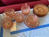 Pink depression glass teacups, saucers, and bread plates with diamond cut pattern and starburst base detail, arranged on a light-colored surface.