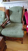 Front view of antique armchair showing light green fabric upholstery, button tufted backrest, carved wood arms and legs.