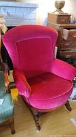 Front-left angled view of magenta fabric antique armchair with solid wood gliding base and wheels.