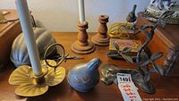 Overall view of brass candlestick holder, metal walnut dish, wooden candle holders, and metal bird sculpture on table