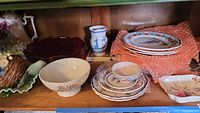 Wide view of shelves with assorted china including plates, bowls, servingware, and a decorative blue and white vase. Items show scratches and wear.