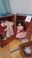 Doll in pink dress secured inside the open wardrobe case, showing the entire lot setup.
