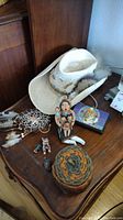 Photo of cowboy hat, dreamcatchers, Native American figurine, decorative box, and small items on wooden surface.