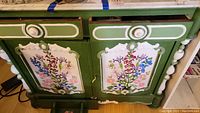 Front view of green hand-painted wooden hutch showing floral painted panels and decorative carved details.