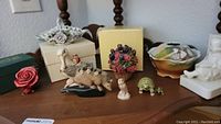 Overview of assorted miniatures and figurines on wooden surface including flower baskets, animal figurines, and a porcelain bowl, showing various pieces and condition.