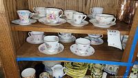 Full shelf view showing two rows with various tea cups and saucers in different floral patterns and colors.