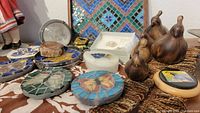 Overview of various trinket boxes, pigeon-shaped wooden figurines, and a white crystal box on a patterned fabric.