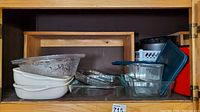 Wide view of cabinet shelf with stacked white ceramic dishes, clear glass Pyrex dishes with floral design, and several loaf pans in the back
