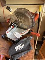 Photo of the circular saw on a wooden workbench showing the dust collection bag and blade guard, side view.
