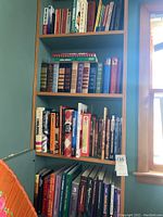 Four shelves filled with assorted books including titles in electronics, communication, physics, and mathematics along a wall beside a window.