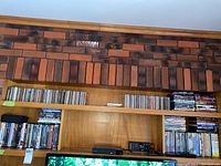 Wide shot of two shelves filled with DVDs and CDs above a TV and electronic devices