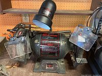 Front view of Craftsman black bench grinder showing grinding wheels with transparent safety guards, product label on motor housing, and on/off switch on base.