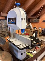 Front and side view of the Delta Shopmaster BS100 band saw showing the body, blue Delta logo, and work table with fence.