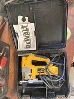 Photo of DeWalt DW321 orbital jig saw inside black hard plastic carrying case with cord and instruction manual visible.