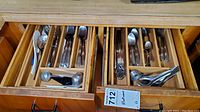Top-down view of three wooden drawers containing the assorted flatware and kitchen utensils separated into compartments.