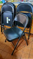 Four black metal folding chairs, three folded and one open, showing sturdy metal seats and backs with folding mechanism.