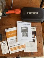 Foxwell branded zippered carrying case, multiple manuals including quick start guide and user manual, and a note describing the device.
