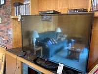 Front view of the LG 42-inch TV showing the screen reflecting a room with couch, lamp, and table.