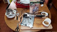 Full lot spread on table showing meat grinder box, BBQ utensils, kitchen tools, and cutting board