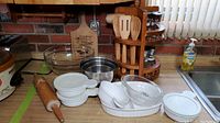 Photo showing the collection of kitchen items including glass mixing bowls, CorningWare crocks with lids, wooden rolling pin, stainless steel bowl, and wooden utensils next to a handcrafted spice rack.