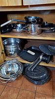 Cabinet with stacked pots and pans, egg poacher, and strainers visible