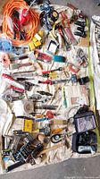 Wide top view of assorted tools spread across a cloth, showing hand and power tools, clamps, hardware, and extension cord.