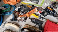 Photo showing assorted hand and power tools, measuring tapes, protective goggles, sanding blocks, utility knives, and electrical cords.