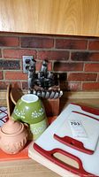 Photo showing Chicago Cutlery knife set in wooden block, two green Pyrex Crazy Daisy bowls stacked, terracotta garlic keeper, and two cutting boards with handles, all on wooden surface.