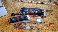 Replica 17th century flintlock pistol, Sarajevo souvenir dagger with sheath, and Roman gladiator style dagger with sheath and wooden stand displayed on carpet.