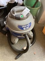 Front and side view of Shop-Vac 6 gallon wet/dry vacuum showing coiled hose, blue body, and gray motor head with label.