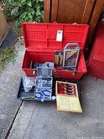 Open red plastic toolbox containing tools shown including Stanley chisel set, pliers, drill bits, screwdriver set, circular saw blade, and assorted metal hardware parts