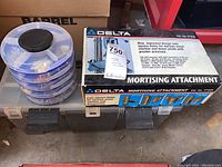 Photo showing Delta mortising attachment box placed on top of a large plastic toolbox with circular storage containers stacked beside it.