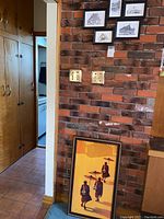 Full view of the framed Burmese monk print leaning against brick wall beside light switches