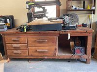 Front left side view of the handmade cedar workbench showing drawers, open storage compartment, and tools on top.