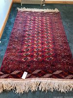 Full view of the wool Turkoman rug laid out, showing the entire surface with red dominant color and fringes on both ends.