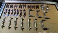 Full assortment of antique style copper and brass drawer pulls and hinges laid out on cardboard surface.
