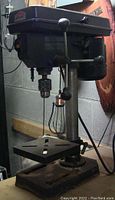 Full view of Jobmate bench top drill press showing base, column, adjustable table and operating handle.