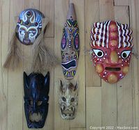 All five masks arranged on wooden floor showing varied styles and materials
