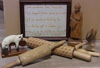 Photo of all items including the wood carving, woodpecker carving, three carved rolling pins, and framed needlework.