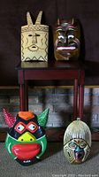 Four assorted masks arranged with two on a table and two below it in front of a fireplace.