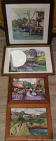 Four framed watercolor paintings displayed on floor, showing distinct scenes of boats, buildings, and street market