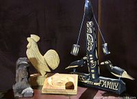 Four folk art carvings on display against black backdrop showing the set including the three birds 'Bless my Family' sculpture, wooden rooster, relief bear plaque, and dog bust with cap.
