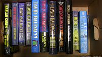 Photo of 11 mystery/crime novels in a box, showing spines with titles and authors. Includes 7 David Baldacci books, 2 Michael Connelly, 1 Lee Child, and 1 Harlan Coben.