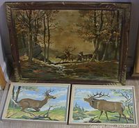 Wide shot showing all three framed paint-by-numbers deer paintings, one large autumn scene above two smaller buck and elk paintings.