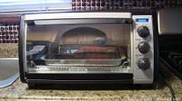Front view of Black and Decker toaster oven showing clear door, wire rack and baking tray inside.