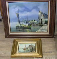 Two framed boat paintings, a larger acrylic by Luini and a smaller oil by T. Travis, displayed on floor.