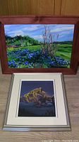 Both original framed paintings shown together; impressionistic landscape with blue flowers and vibrant greenery on top, abstract mountain painting below with mat and silver frame.