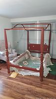 Front angle view of the full-sized 4 poster bed with brick red wooden frame and handmade diamond pattern rope canopy laid inside the bed frame.